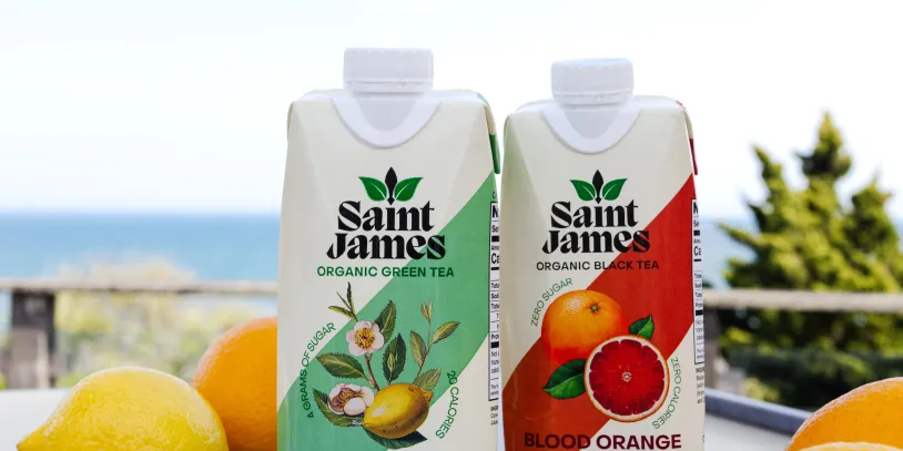 Two juice cartons labeled "Saint James" alongside lemons and oranges, set on a table with a sea view in the background.