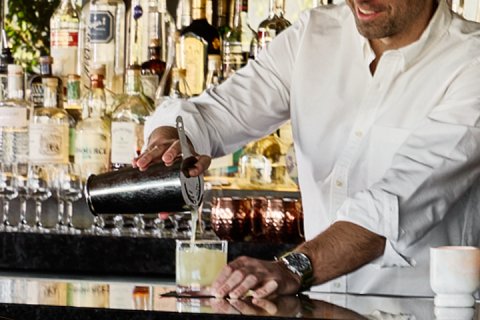 Bartender pouring shaken cocktail into glass.