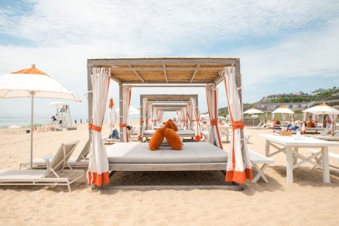 Private beach cabana with orange accents, lounge chairs and umbrella.