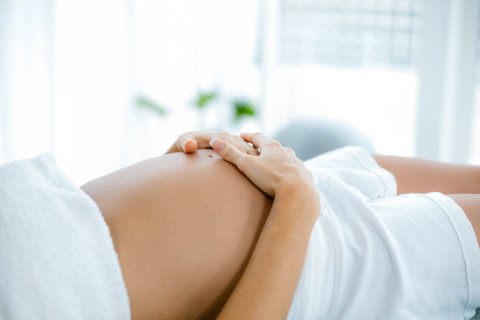 Pregnant woman relaxing on massage table with hands resting on her belly.