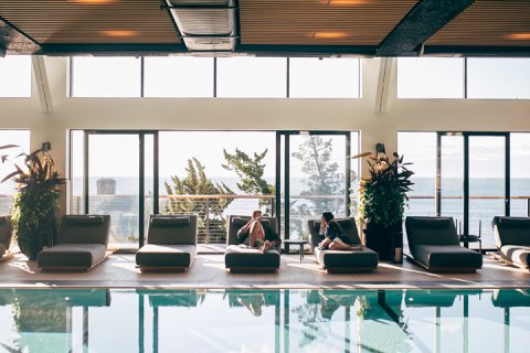 Couple in robes relaxing on lounge chairs beside Seawater Spa's indoor pool.