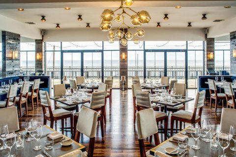 Scarpetta Beach Dining room with wood floors, floor to ceiling windows with ocean view, and tables set for dinner.