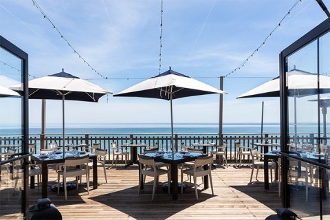 Three dining tables with sun umbrellas line the ocean-facing deck at Scarpetta Beach in Montauk