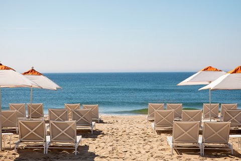 Rows of gray lounge chairs and white and orange umbrellas face the ocean at Gurney's Montauk beach club
