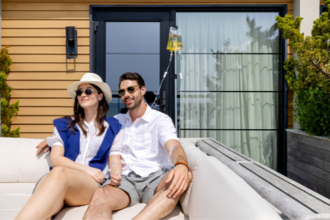 A couple lounges together outdoors while receiving saline IV drips.