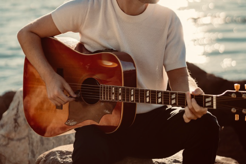 A closeup of a man holding a guitar with water in the background