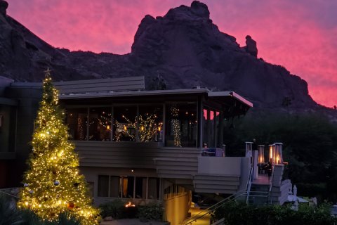 Christmas Tree with holiday lights in front of elements with pink sunset and Praying Monk in background.