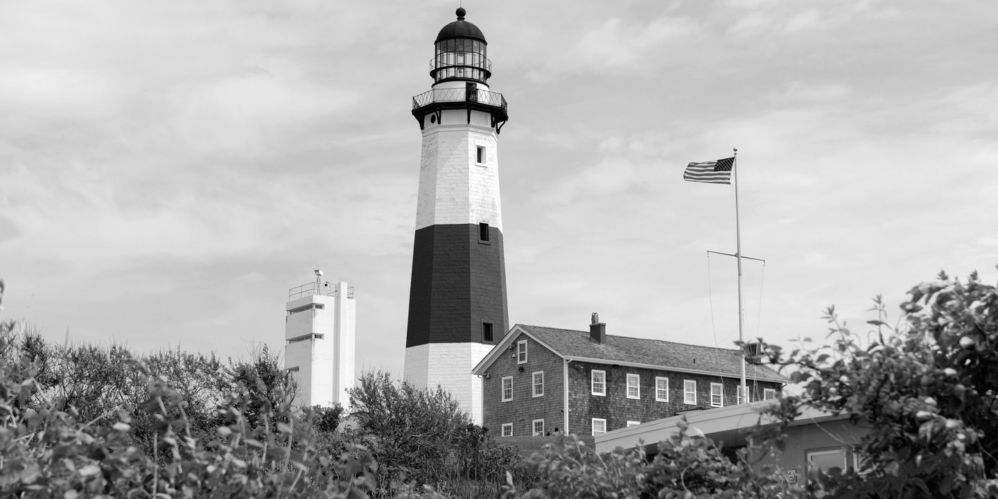 Black and white photo from across field of Montauk lighthouse and surrounding  buildings.