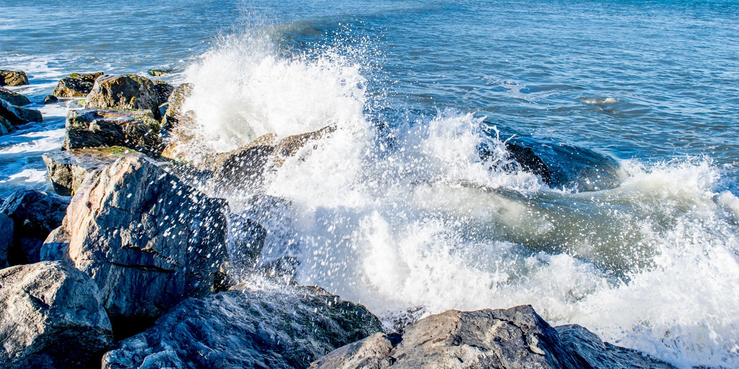 Close up of white water waves splashing against rocky shoreline.