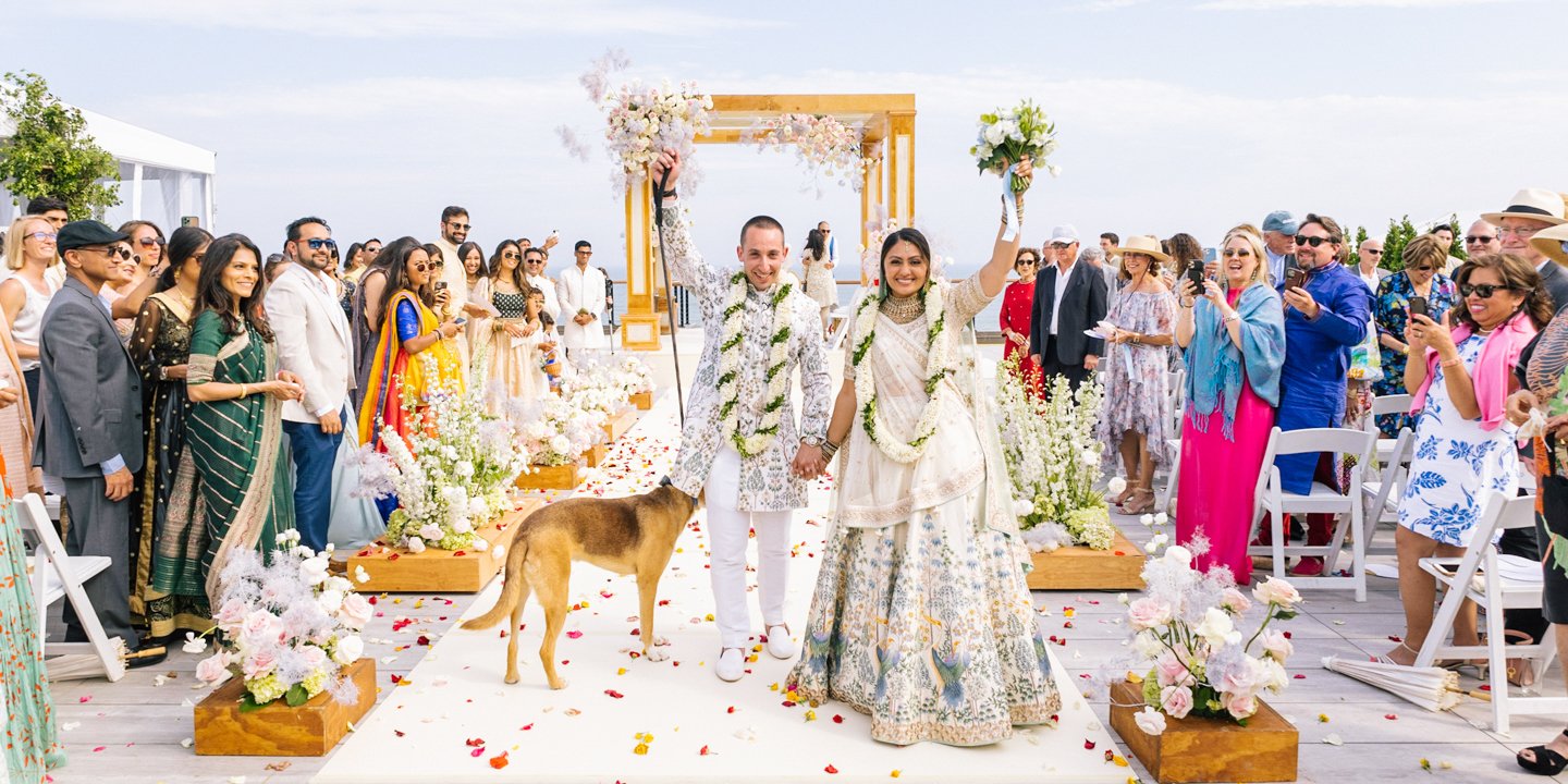 Bride and Groom with dog walking down the aisle celebrating as friends and family cheer after wedding ceremony.