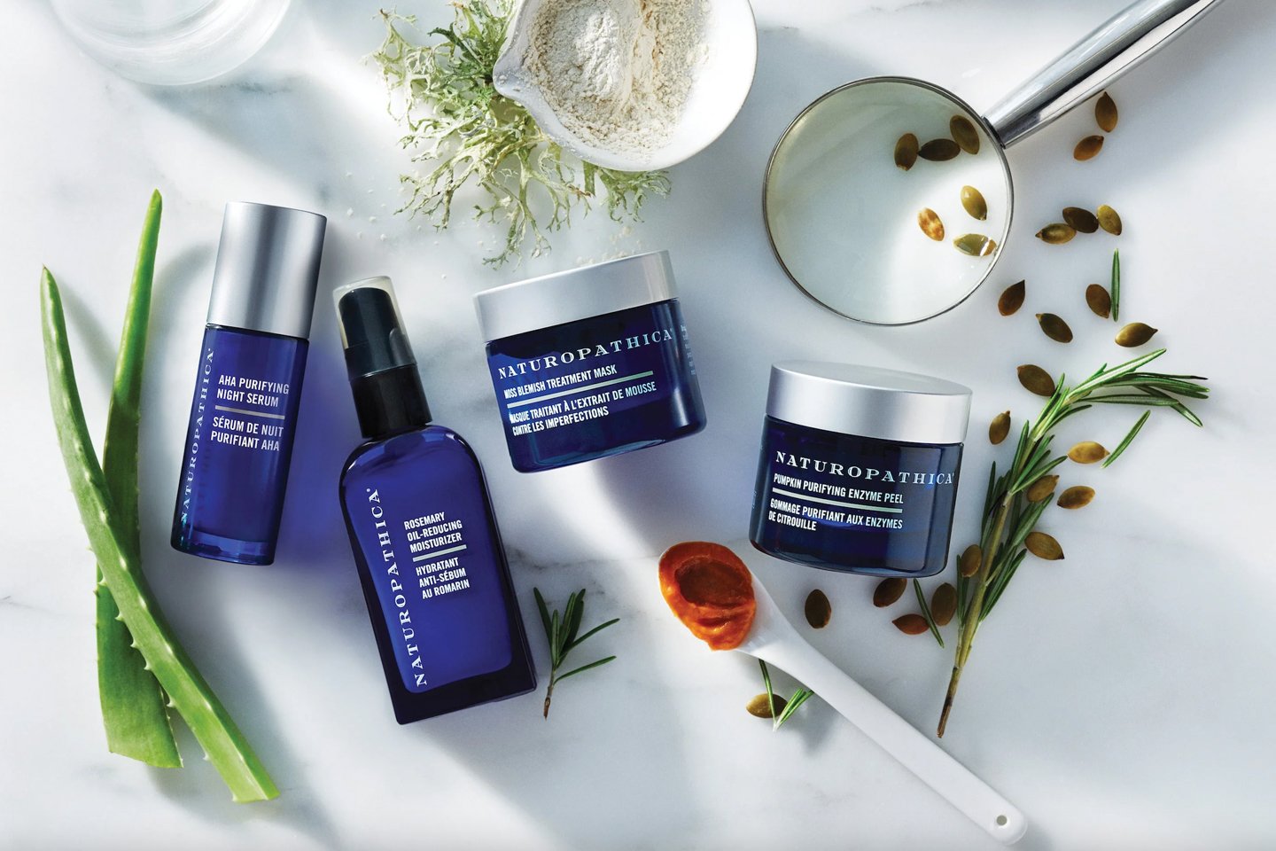 An array of Naturopathic skin products in blue packaging surrounded by fresh ingredients like aloe and collagen.