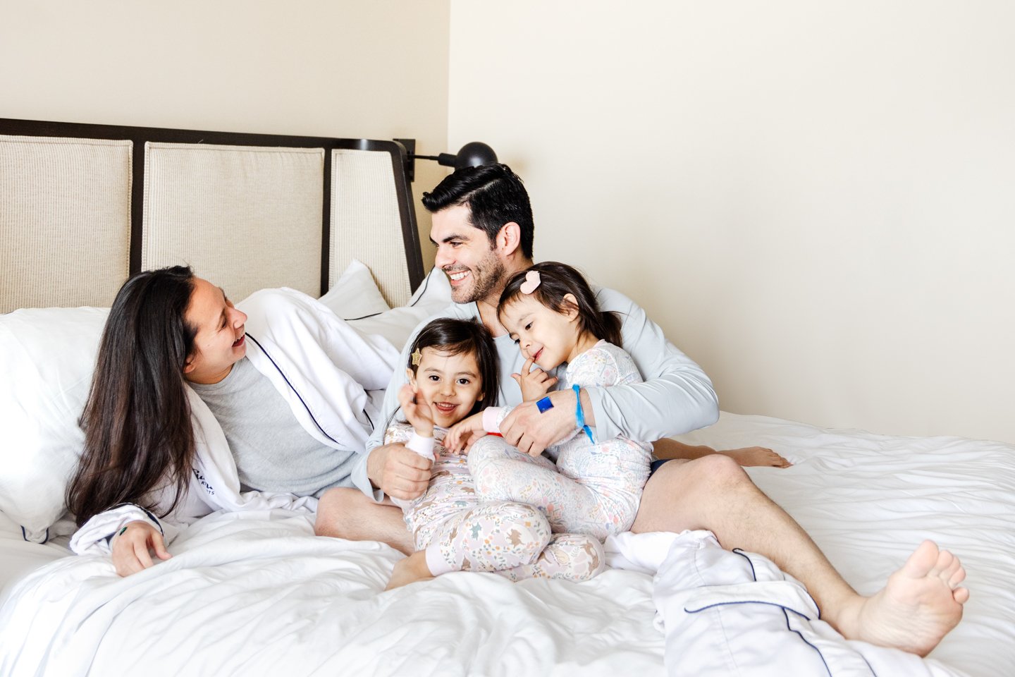 Husband and wife laughing in bed while cuddling with their two young daughters.
