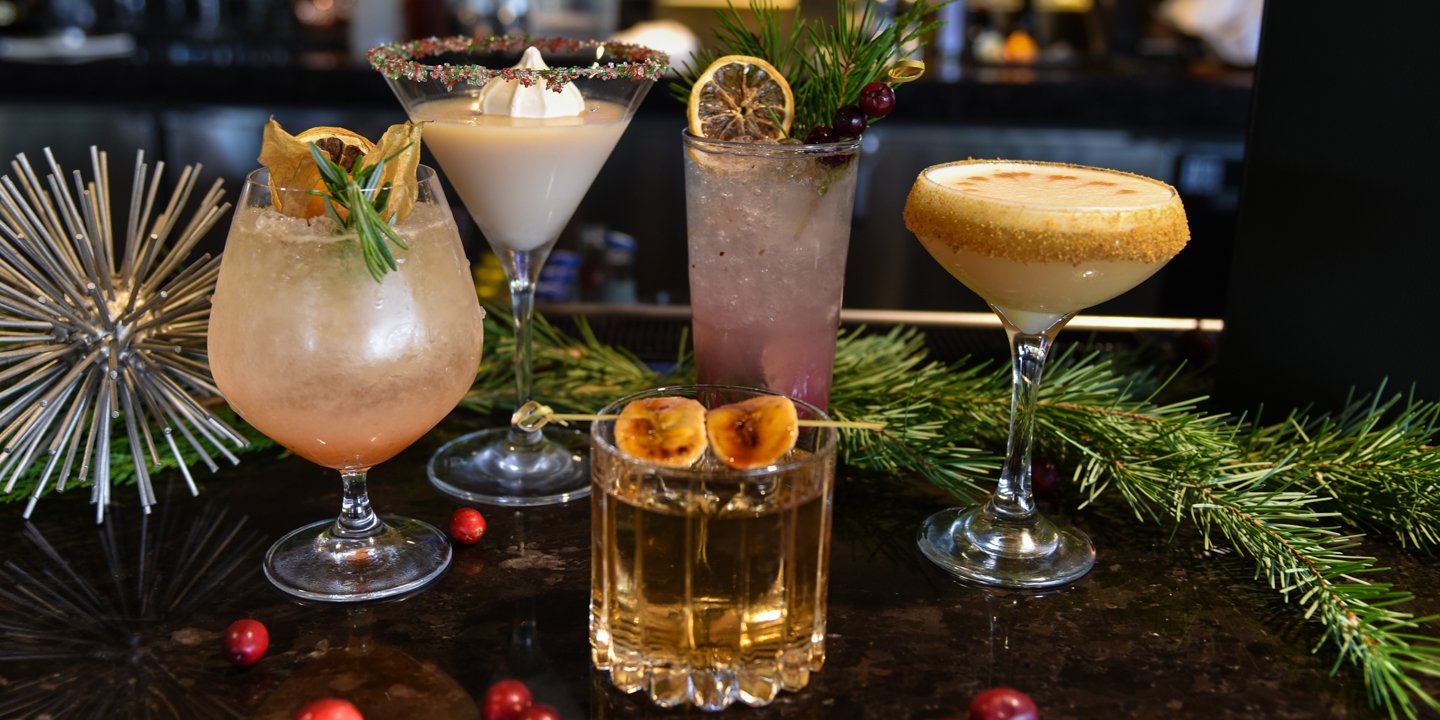 Five of Jade Bar's 12 Days of Cocktails creations in a variety of glassware surrounded by holiday decor.
