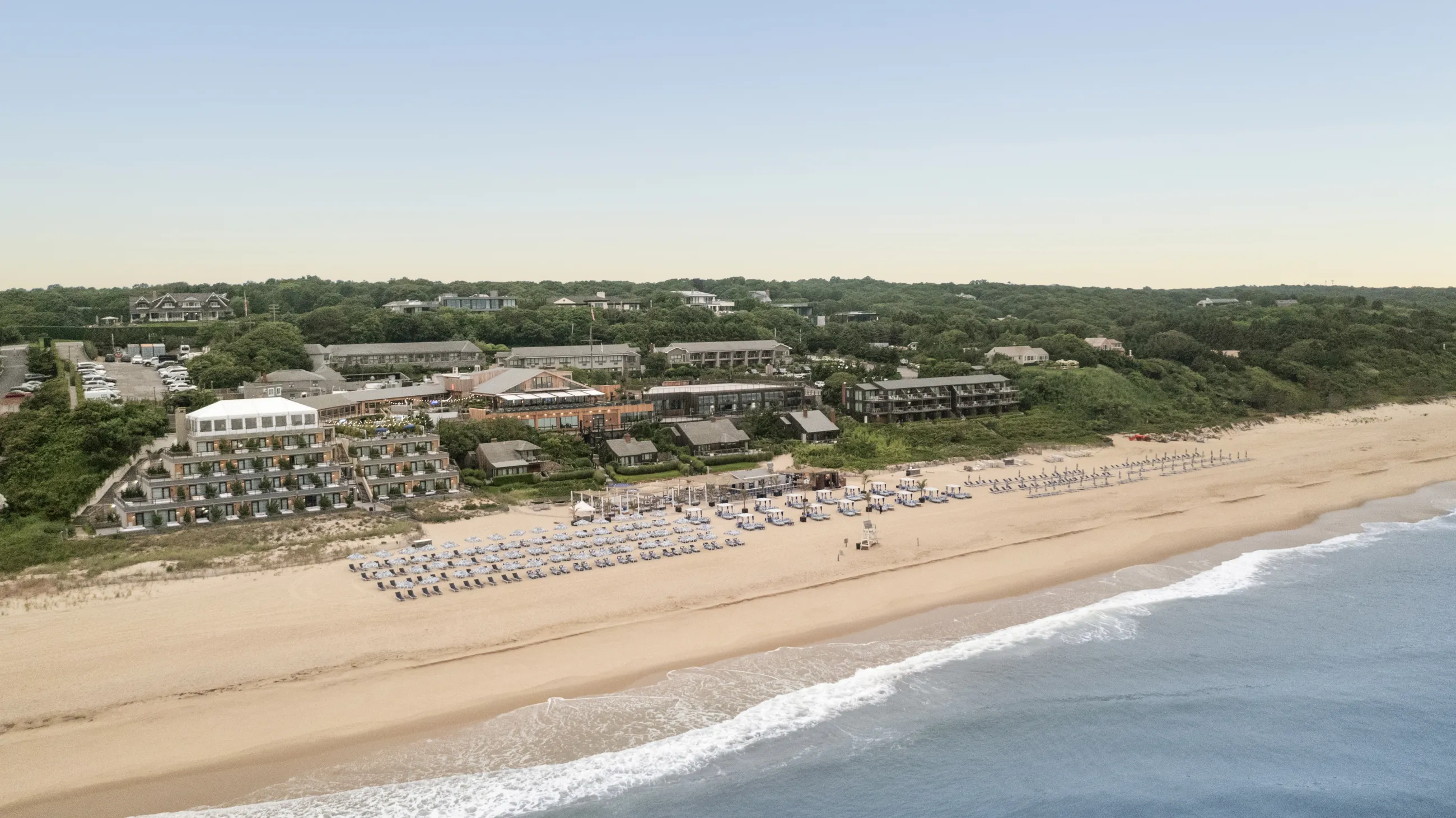 Aerial view of a beachfront resort with buildings, trees, and a beach.