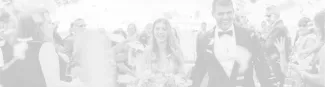 A bride and groom smile as they walk through a crowd of celebrating guests holding flowers.