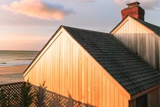 Sunset reflecting off the wood side of a building with the ocean and beach in the backround