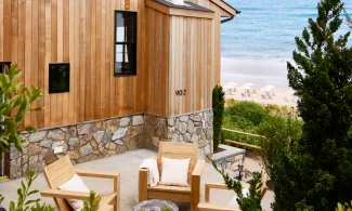 Wooden patio with cushioned chairs, lush green plants, and a sea view in the background.