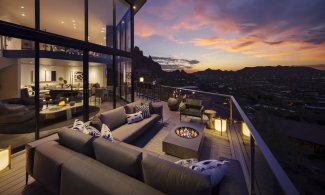Wrap-around outdoor deck with couch and fire pit overlooking valley at dusk.