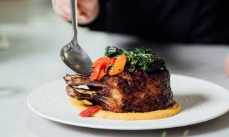 Bone-in pork chop being sauced by chef during plating.
