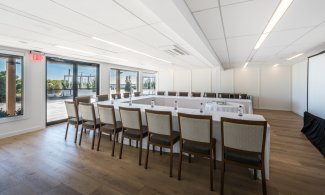 Latitude with wood floor, white walls, u-shaped table setup with white linens, projector and screen.