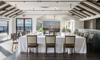 The Regent Lounge with wood floors, white walls and ceiling with wooden accents, u-shaped table setup with white linen and television with Gurney’s Logo on screen.