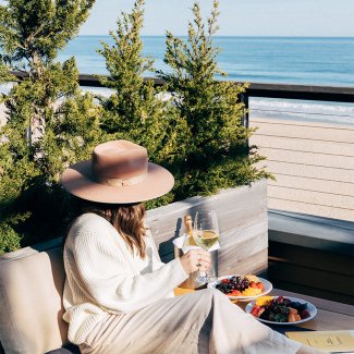 A woman in a hat looks out onto the ocean while holding a glass of white wine at Gurney's Montauk Resort