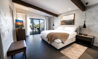 Mountain Suite King with accent wall with art, nightstand with light, flatscreen television, dresser and wrap around patio.