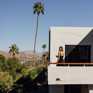 Woman standing on balcony of casita holding a glass of red wine and enjoying the view.