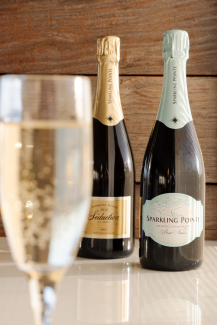 A glass of sparkling wine in the foreground and two bottles of Sparkling Pointe wine in the background