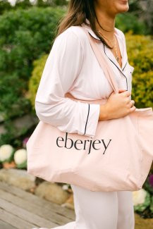 A woman in pink pajamas carries an Eberjey tote with Gurney's Montauk in the background