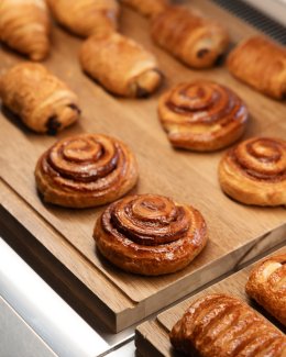 Freshly baked pastries, including golden-brown cinnamon rolls and croissants, arranged on a wooden tray.