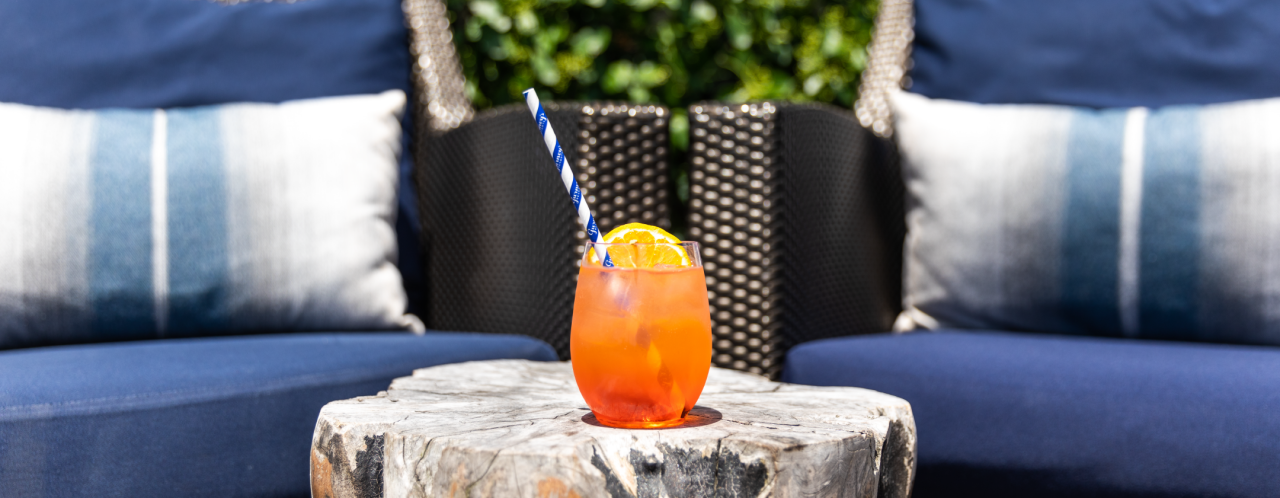 An orange cocktail sits in front of a pair of matching blue cushioned chairs at the Gurney's Montauk Firepit